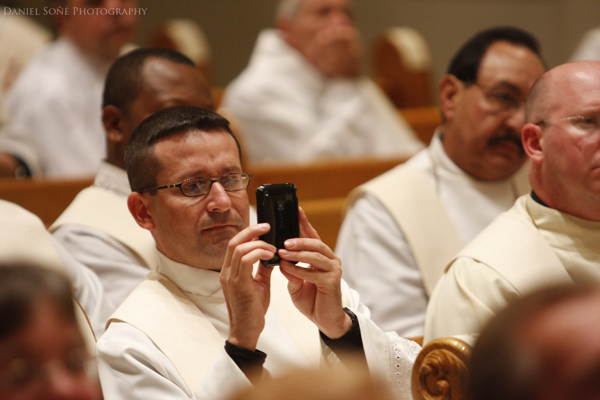 A priest records bishop-elect Fernando Isern's speech on cellphone.
